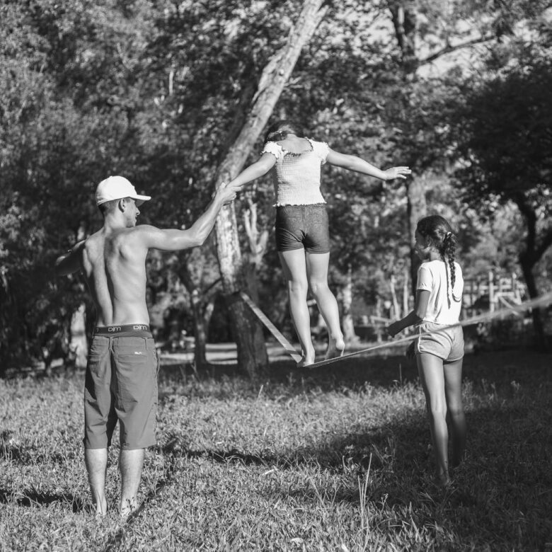 man and girls walking on line between trees in black and white